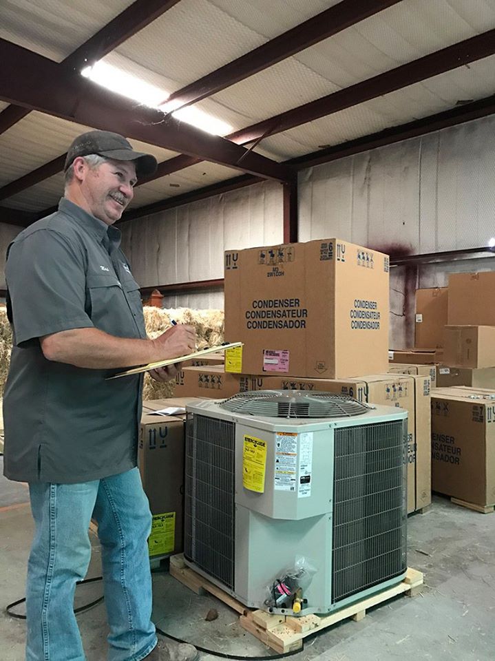 Johnson Mechanical Services technician inspecting a new HVAC condenser unit in the Brownwood, TX warehouse before a job